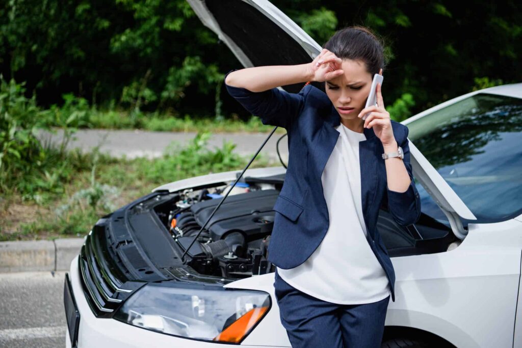 mulher falando no celular com carro quebrado ao fundo