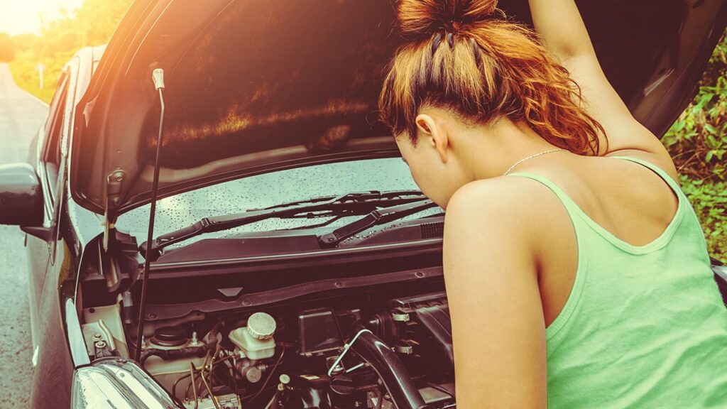 Mulher olhando para o motor de um carro com defeito - motor de arranque