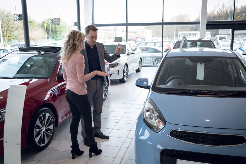 Vendedor mostrando carro para compradora em loja de veículos - - tipos de financiamento - financiamento de veículos