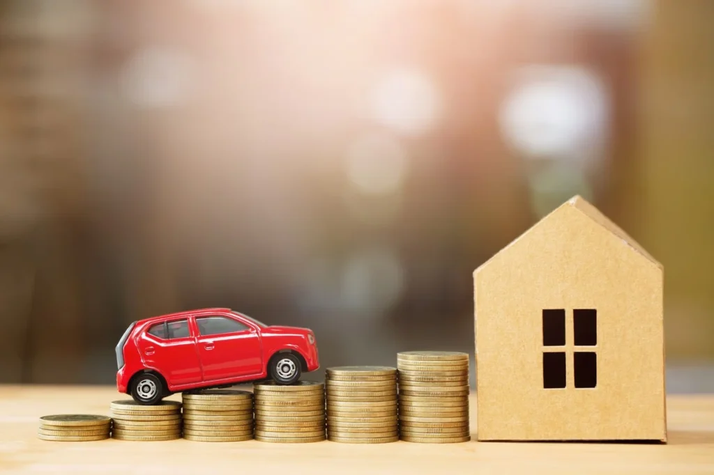 Melhor banco para financiar veículo em 2025: descubra as opções ideais 4 Miniatura de carro vermelho sobre pilhas de moedas ao lado de uma casa de papelão, simbolizando financiamento; ideal para ilustrar conteúdos sobre o melhor banco para financiar veículo
