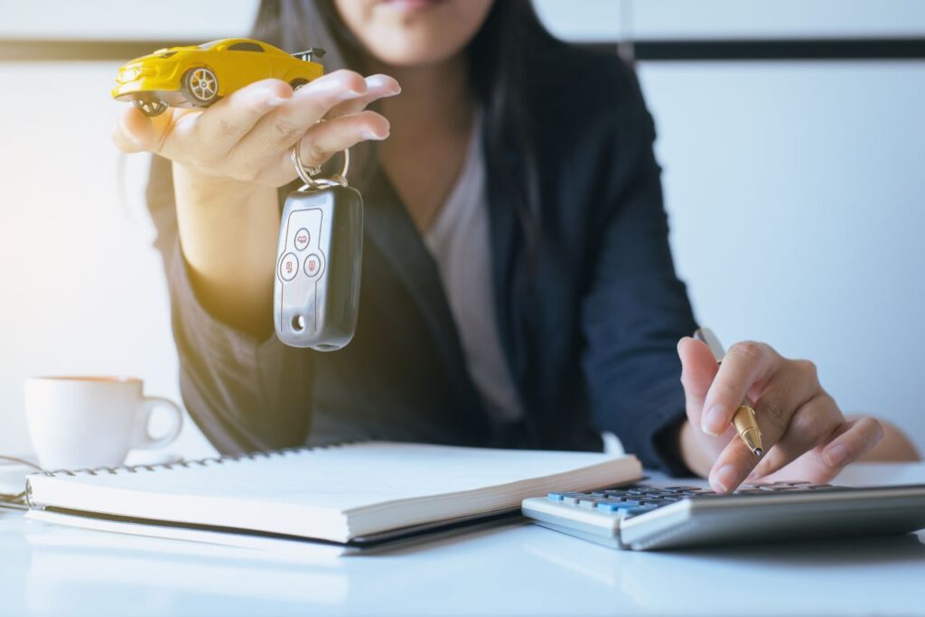 por que os carros estão tão caros - mulher segurando chave na mão e um carrinho de brinquedo amarelo e fazendo contas