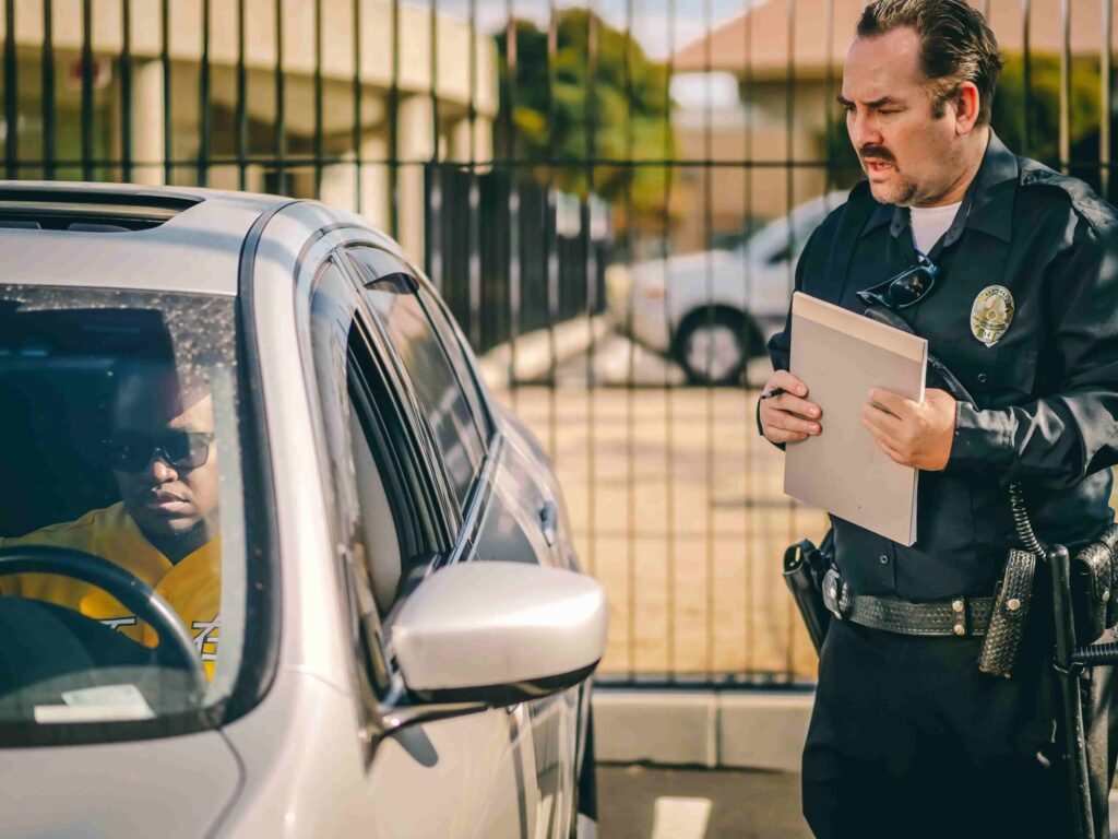 Imagem de um guarda aplicando uma multa em uma pessoa que está em um carro.