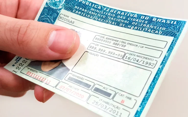 Pessoa segurando uma carteira de motorista brasileira (CNH) parcialmente preenchida, exibindo dados como nome, data de nascimento, CPF e validade do documento