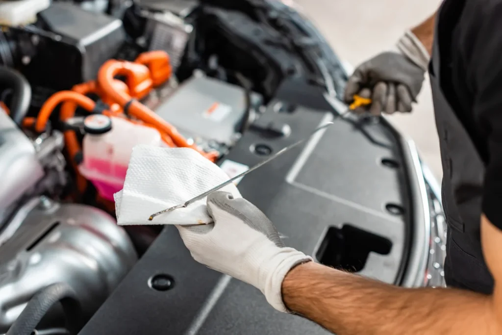 Mecânico verificando as especificações de óleo de motor ao inspecionar o nível com a vareta no compartimento do motor de um carro.