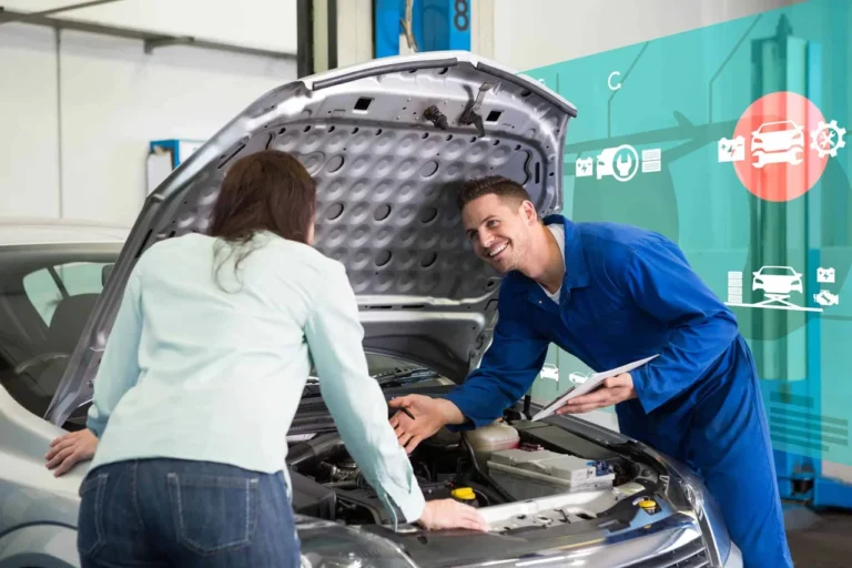 Mecânico sorridente conversa com cliente enquanto verifica o motor de um carro em uma oficina, representando a importância do histórico de revisões para a manutenção preventiva - motor ciclo miller